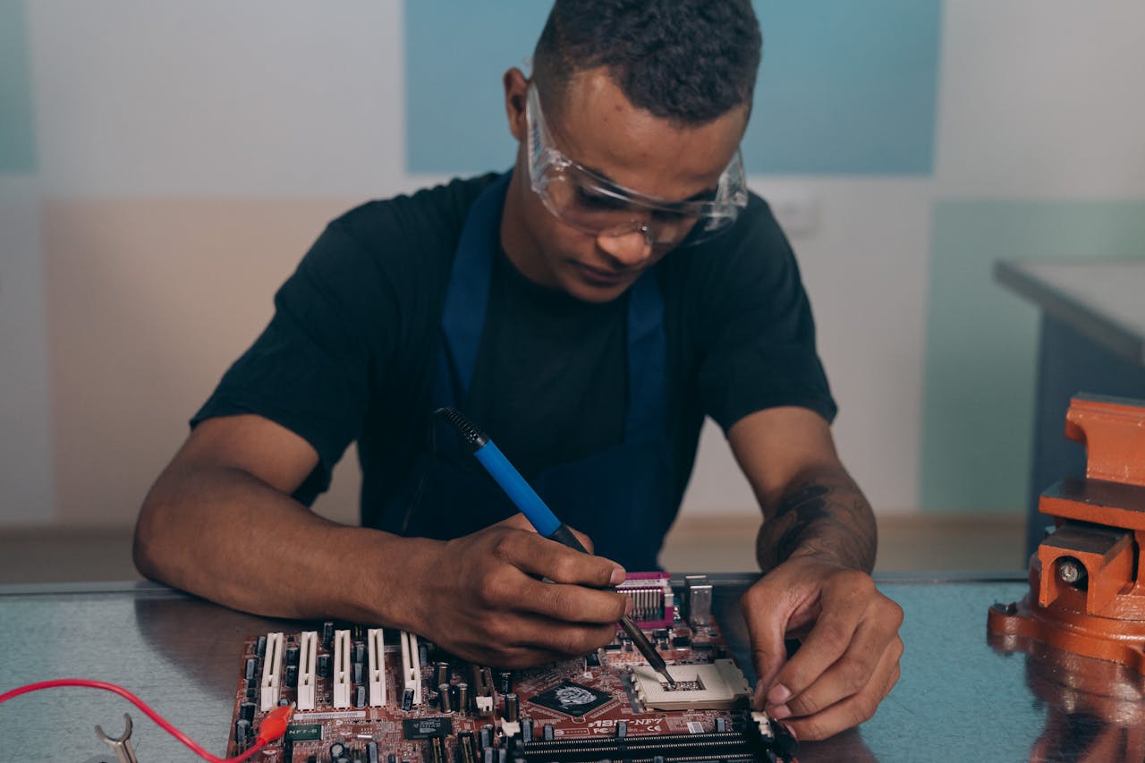 services-06 A technician wearing safety glasses works intently on a computer motherboard with a soldering iron.